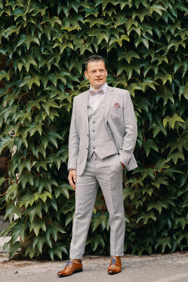 Homme de face en costume SUAT gris à carreaux 3 pièces dans une cours. Il porte des chaussures marrons.