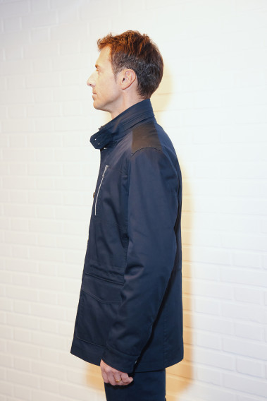 Homme de profil portant la Parka ANNA marine. Elle comporte une poche poitrine, 2 poches plaquées avec rabat.