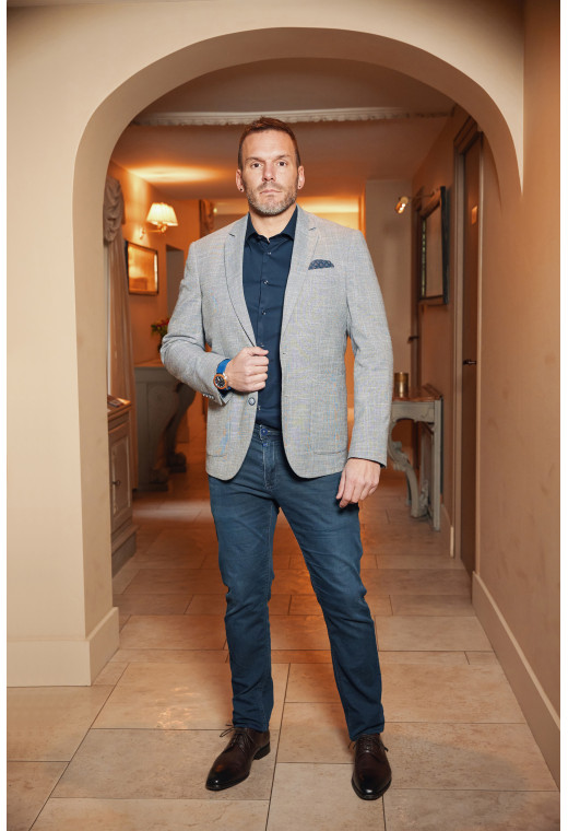 Homme portant la veste SELENA bleue. Elle comporte une poche poitrine et 2 poches plaquées.