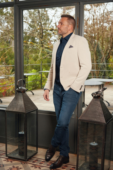 Homme portant la veste VALENTINA beige. Elle comporte une poches poitrine et 2 poches plaquées.