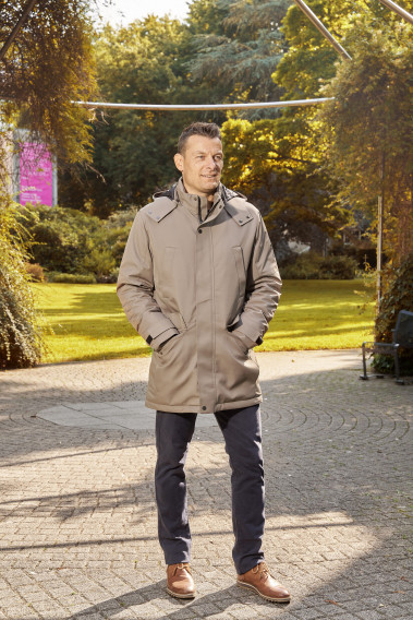 Homme portant la parka SIERA beige. Elle comporte 4 poches et un lien de serrage à la taille.