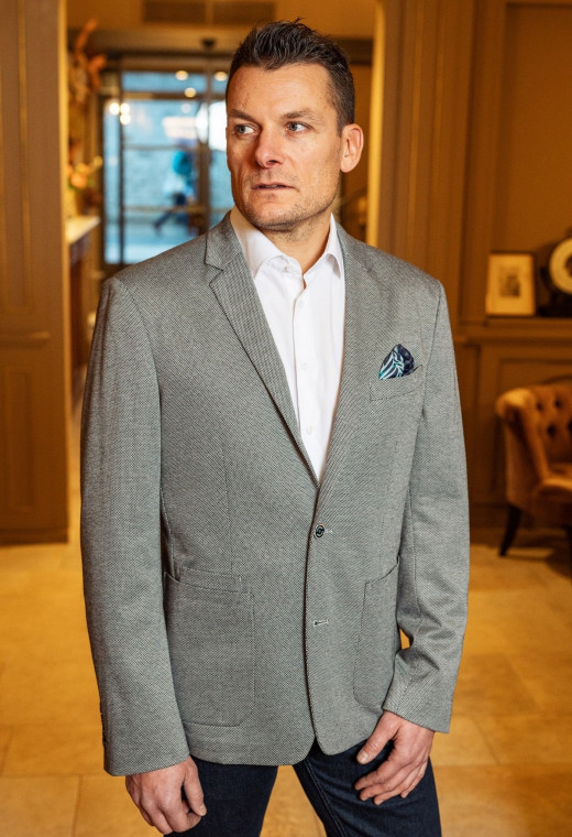 Homme portant la veste JEFF grise. Elle comporte une poche poitrine et 2 poches plaquées.