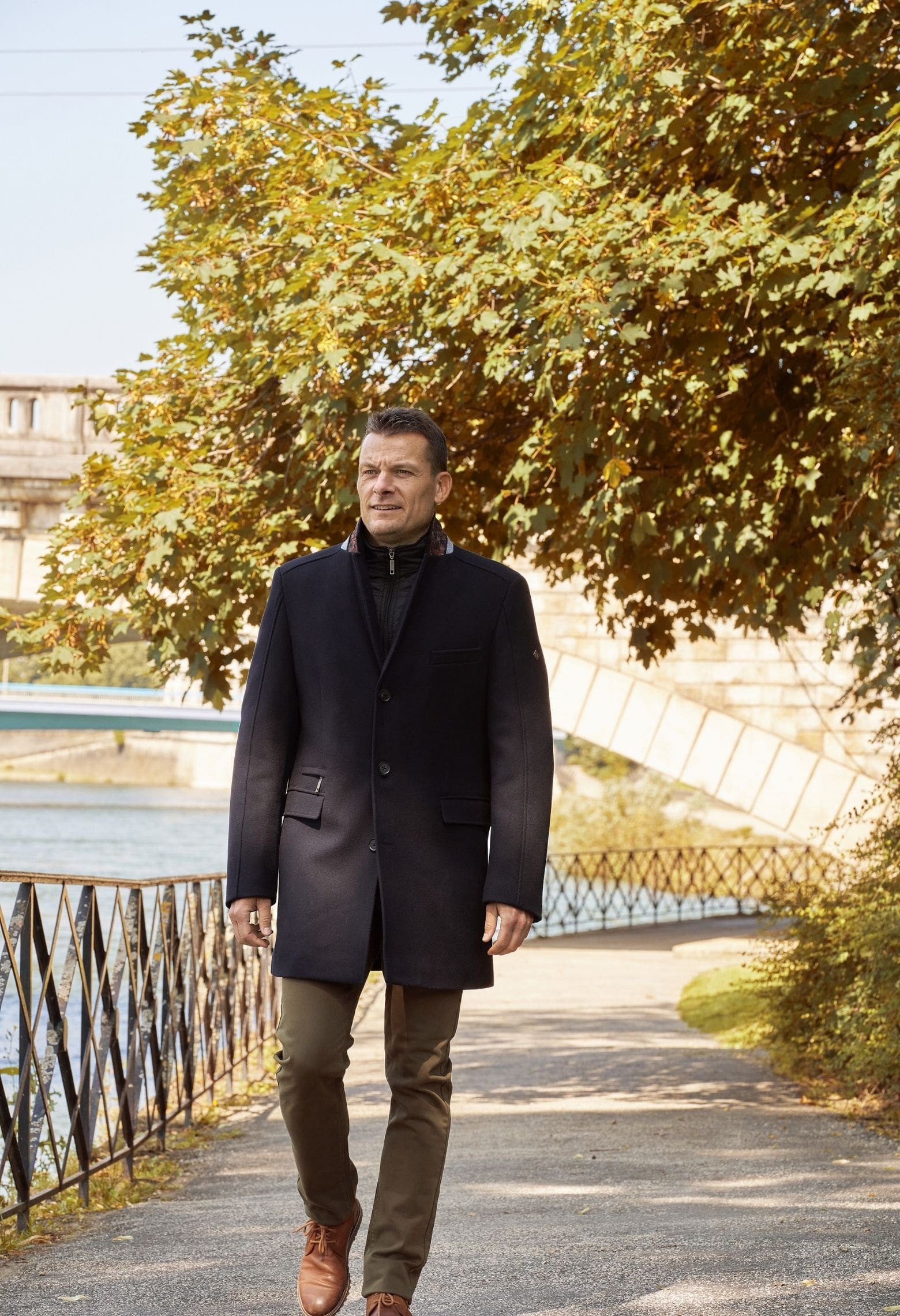 Homme portant le manteau AZARIA marine. Il est long et comporte une poche poitrine et 2 poches repose mains.