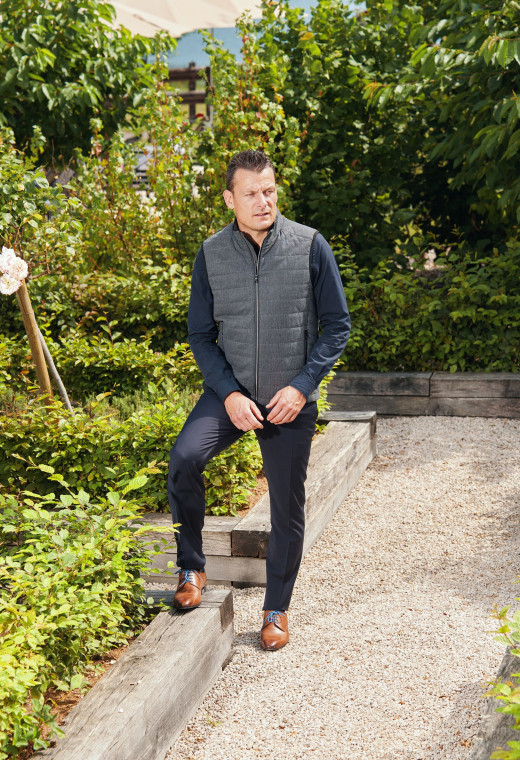 Homme portant la doudoune sans manche KOS grise. Elle comporte 2 poches repose mains.