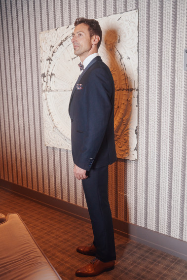 Homme de profil en smoking CELESTEC couleur marine 3 pièces dans une maison. Il porte des chaussures marrons.