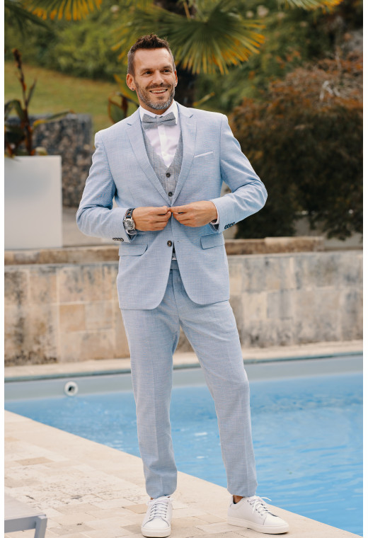Homme de face en costume DIANA couleur bleu clair 3 pièces devant une piscine.