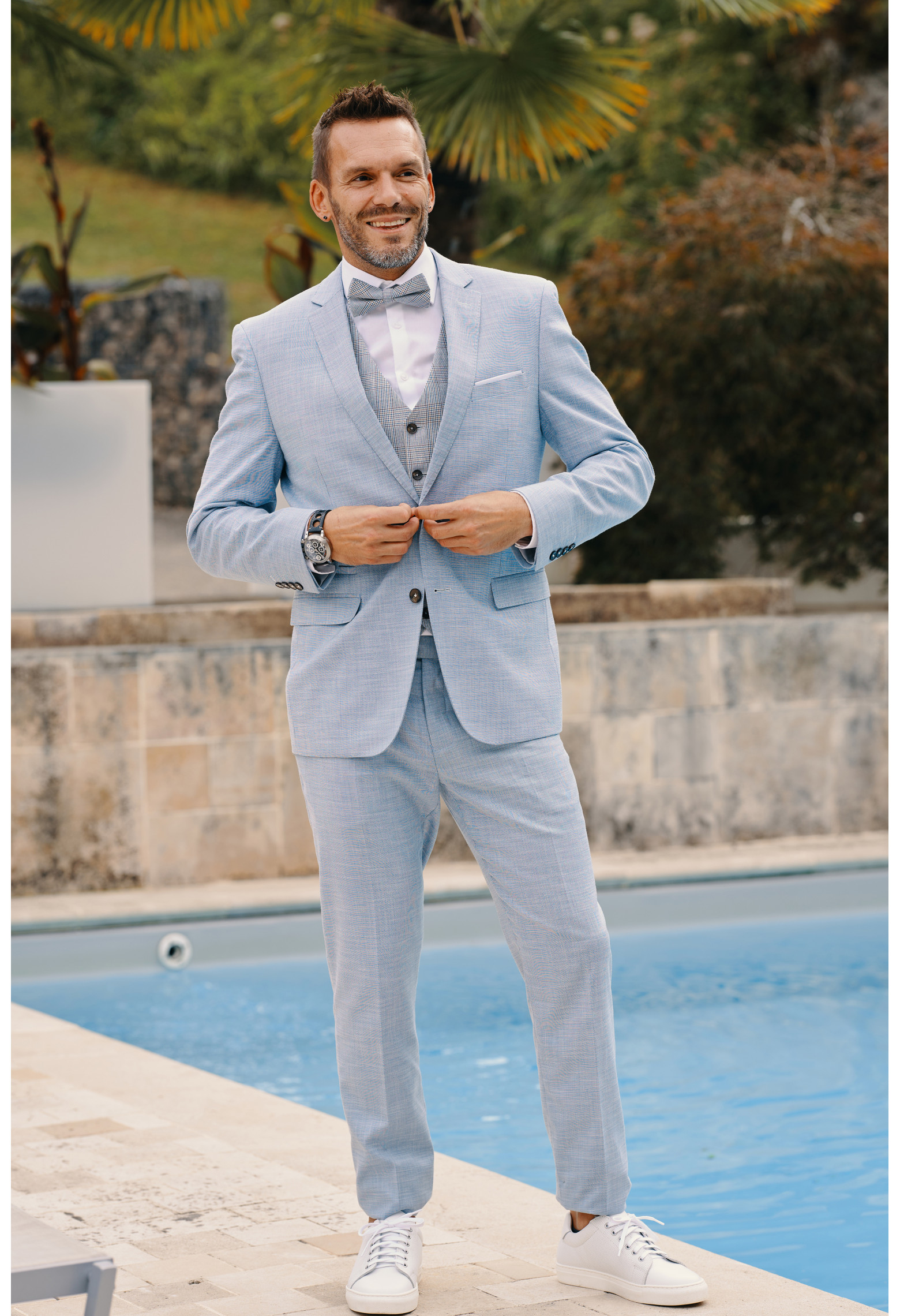 Homme de face en costume DIANA couleur bleu clair 3 pièces devant une piscine.