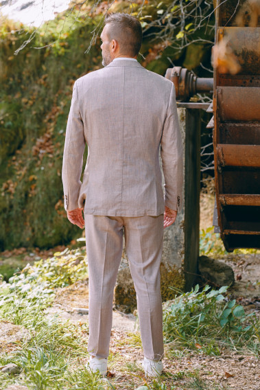 Homme de dos en costume GIORGIO couleur rose poudré 3 pièces dans une cours. Il porte baskets blanches.