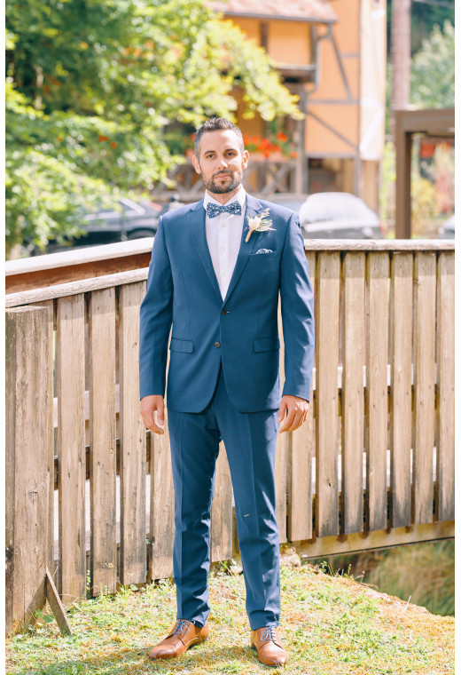 Homme de face en costume SUAT couleur bleu 2 pièces sur un balcon.