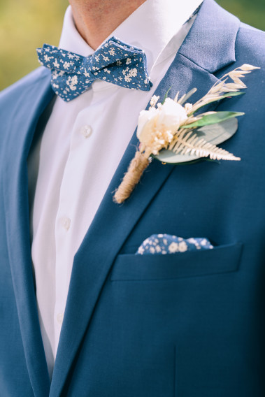 Costume SUAT bleu. Plan sur le nœuds  papillon bleu à motif florale et son mouchoir de poche ainsi qu'un pins.