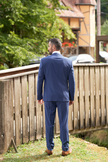 Homme de dos en costume SUAT couleur bleu 2 pièces sur un balcon. Il porte des chaussures marrons.