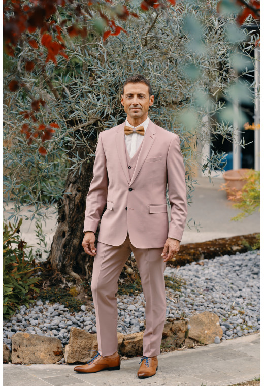 Homme de face en costume SUAT rose 3 pièces dans une cours.