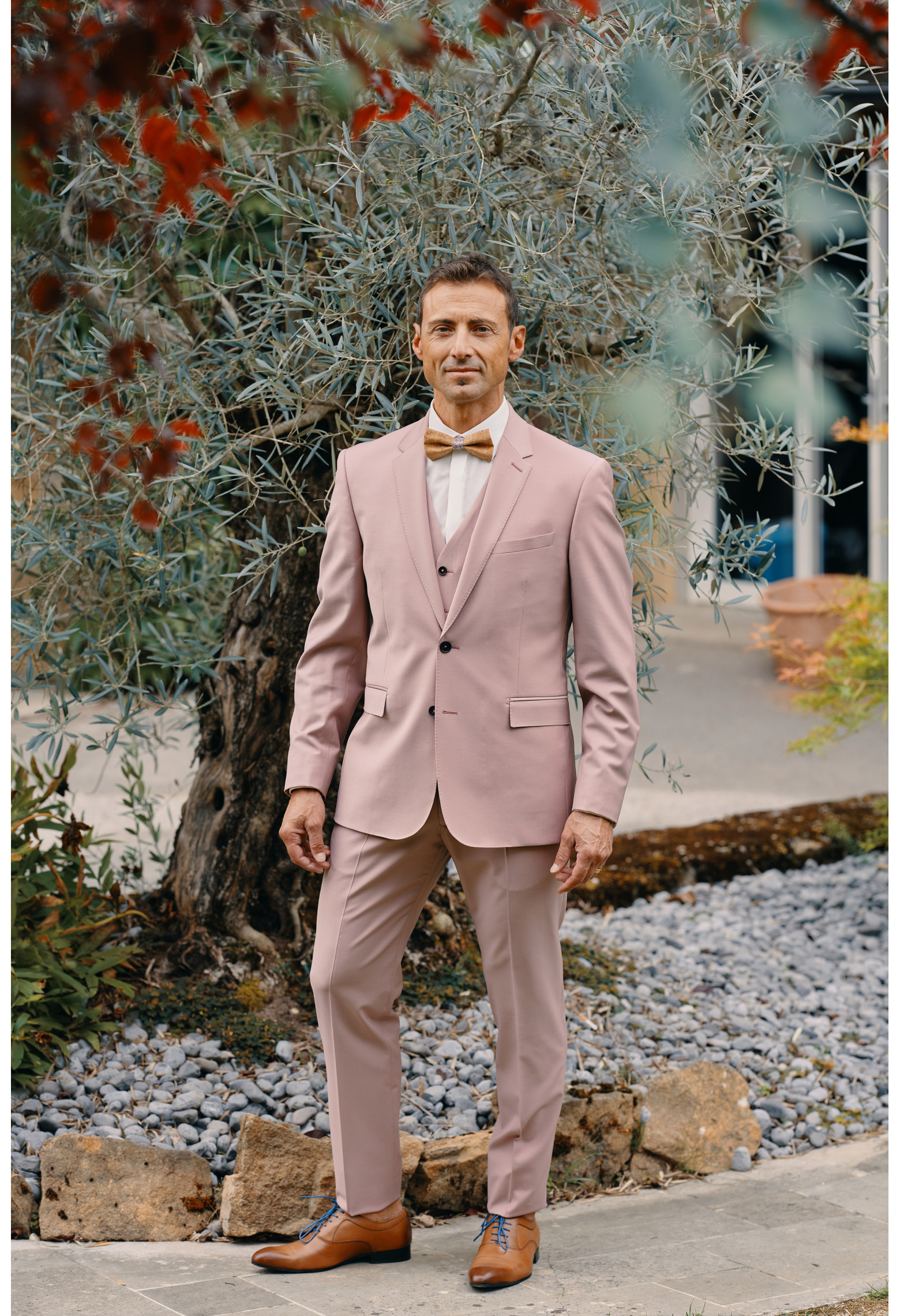 Homme de face en costume SUAT rose 3 pièces dans une cours.