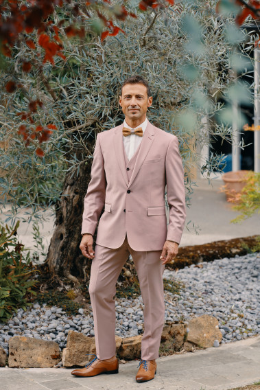 Homme de face en costume SUAT rose 3 pièces dans une cours.