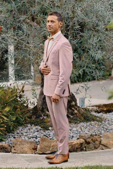 Homme de profil en costume SUAT rose 3 pièces dans une cours.