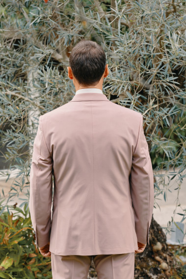 Homme de dos en costume SUAT rose 3 pièces dans une cours. Il porte des chaussures marrons.