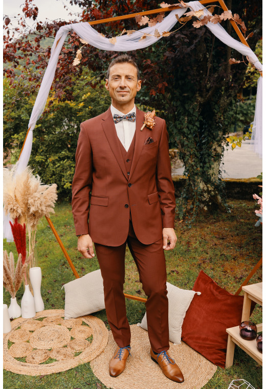 Homme de face en costume SUAT couleur terracotta 3 pièces dans une cours.