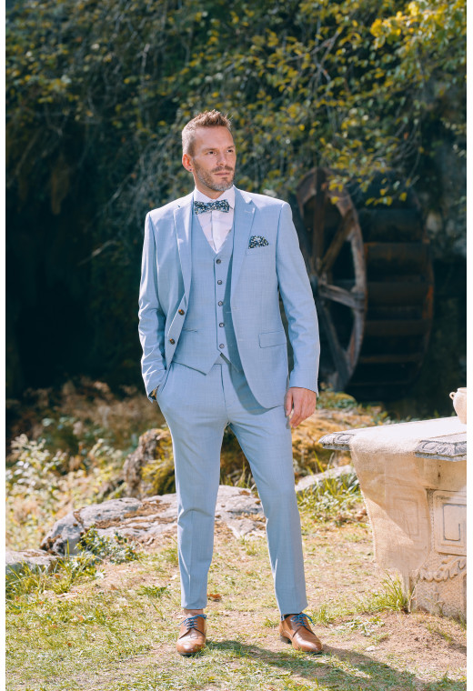 Homme de face en costume SUAT couleur bleu pastel 3 pièces près d'une cascade.