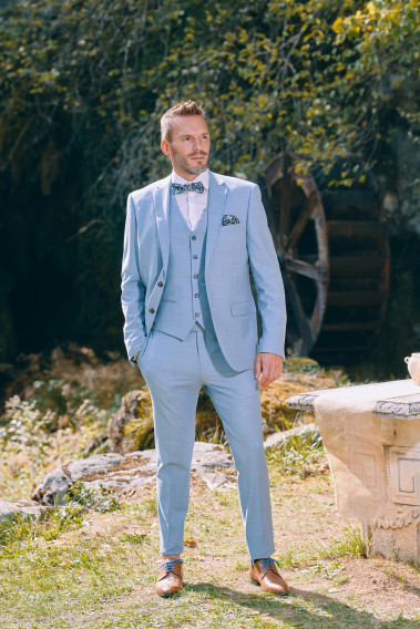 Homme de face en costume SUAT couleur bleu pastel 3 pièces près d'une cascade.