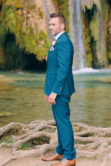 Homme de profil en costume SUAT couleur bleu-vert 3 pièces vers une cascade.
