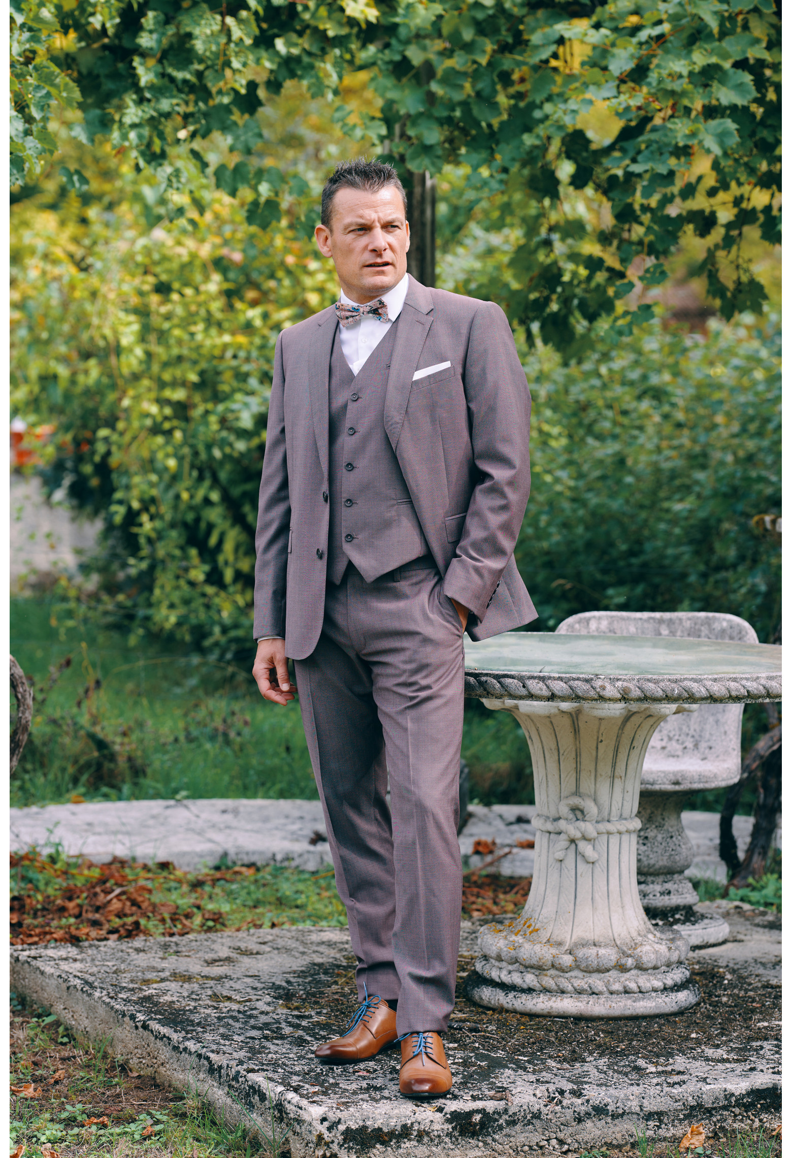 Homme de face en costume SUAT rose-violet 3 pièces une cours. Il porte des chaussures marrons.