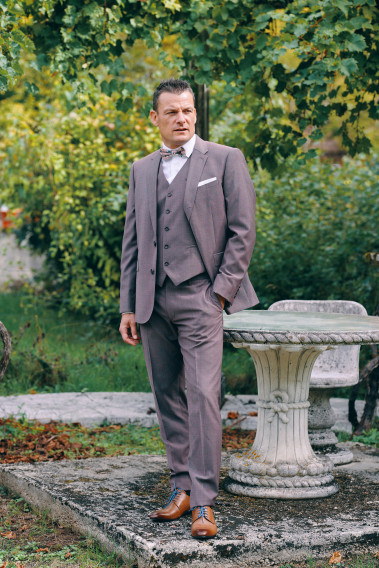 Homme de face en costume SUAT rose-violet 3 pièces une cours. Il porte des chaussures marrons.