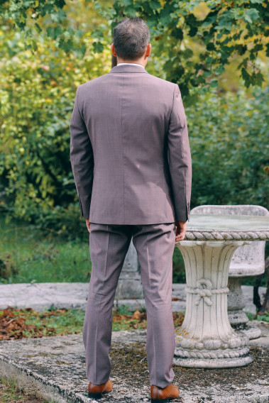 Homme de dos en costume SUAT rose-violet 3 pièces une cours. Il porte des chaussures marrons.