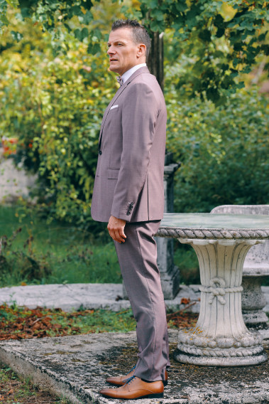 Homme de profil en costume SUAT rose-violet 3 pièces une cours. Il porte des chaussures marrons.
