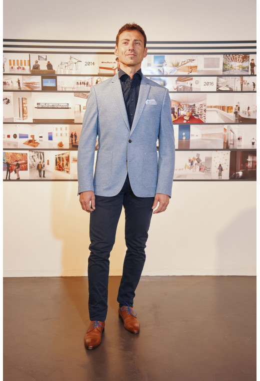 Homme portant la veste VALENTINA bleu clair. Elle comporte une poche poitrine et 2 poches plaquées.
