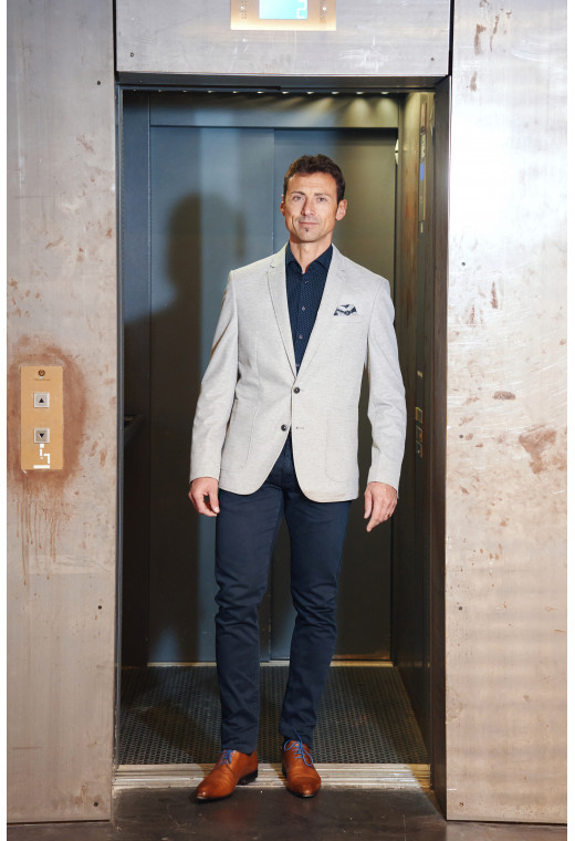 Homme portant la veste VALENTINA gris clair. Elle comporte une poche poitrine et 2 poches plaquées.