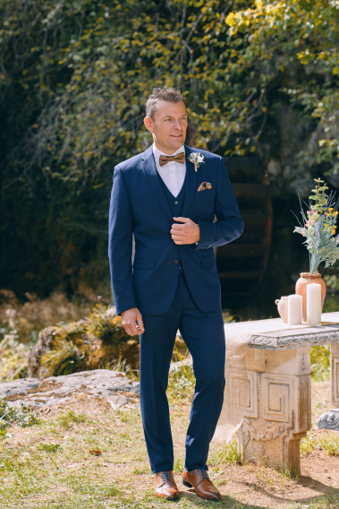 Homme de face en  Costume SUAT micro dessin couleur  marine 3 pièces devant une cascades.