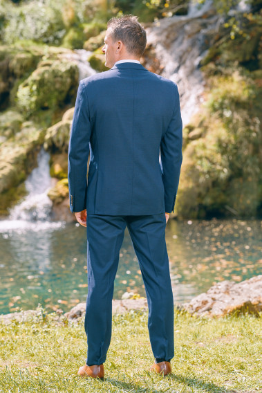 Homme de dos en  Costume SUAT micro dessin couleur  marine 3 pièces devant une cascades. Il porte des chaussures marrons.