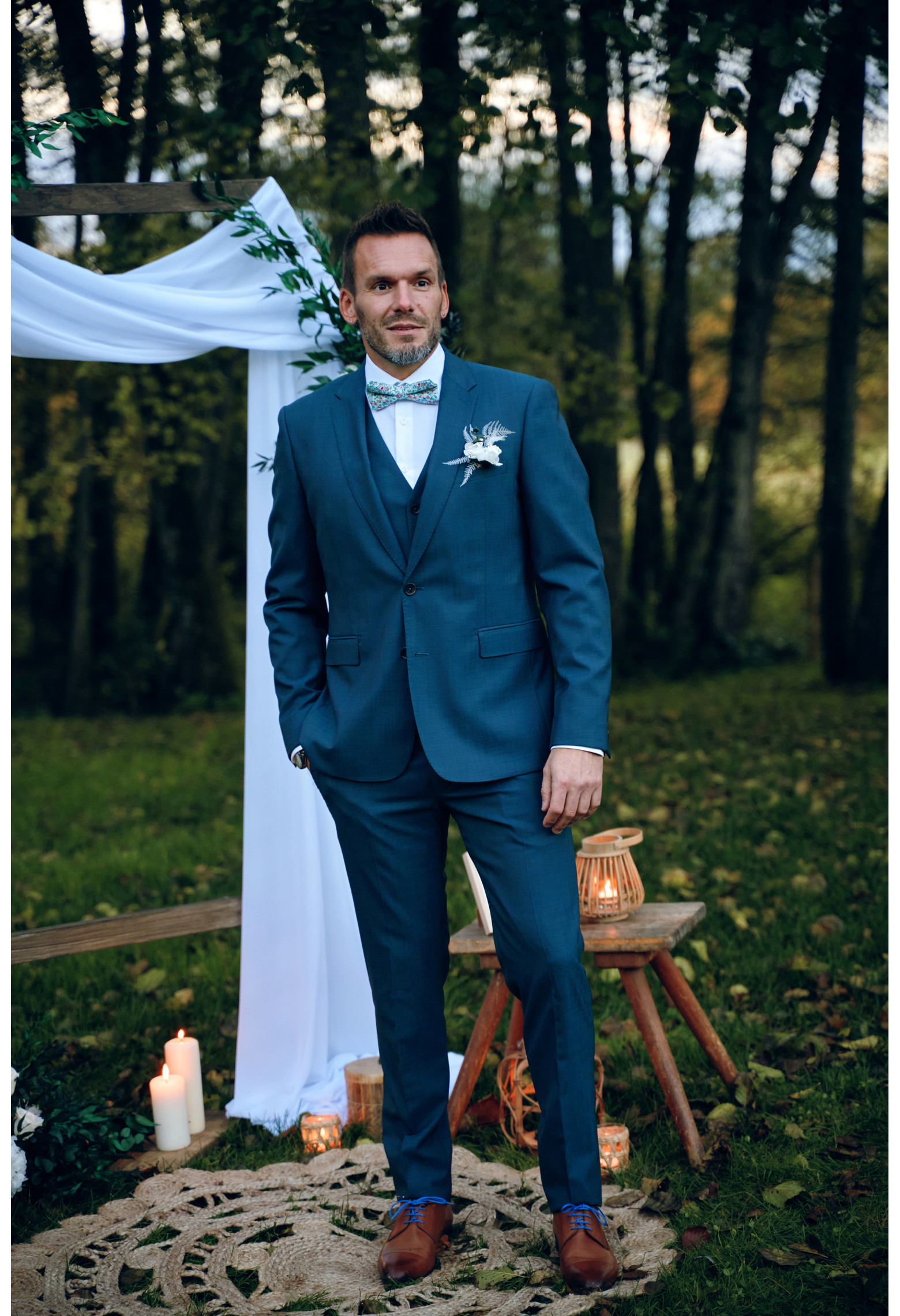 Homme de face en costume SUAT couleur vert-bleu 3 pièces dans une cours .