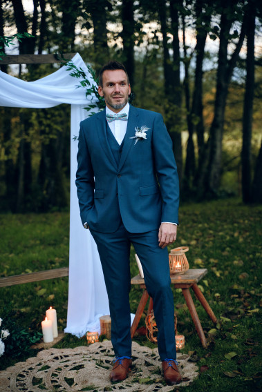 Homme de face en costume SUAT couleur vert-bleu 3 pièces dans une cours .