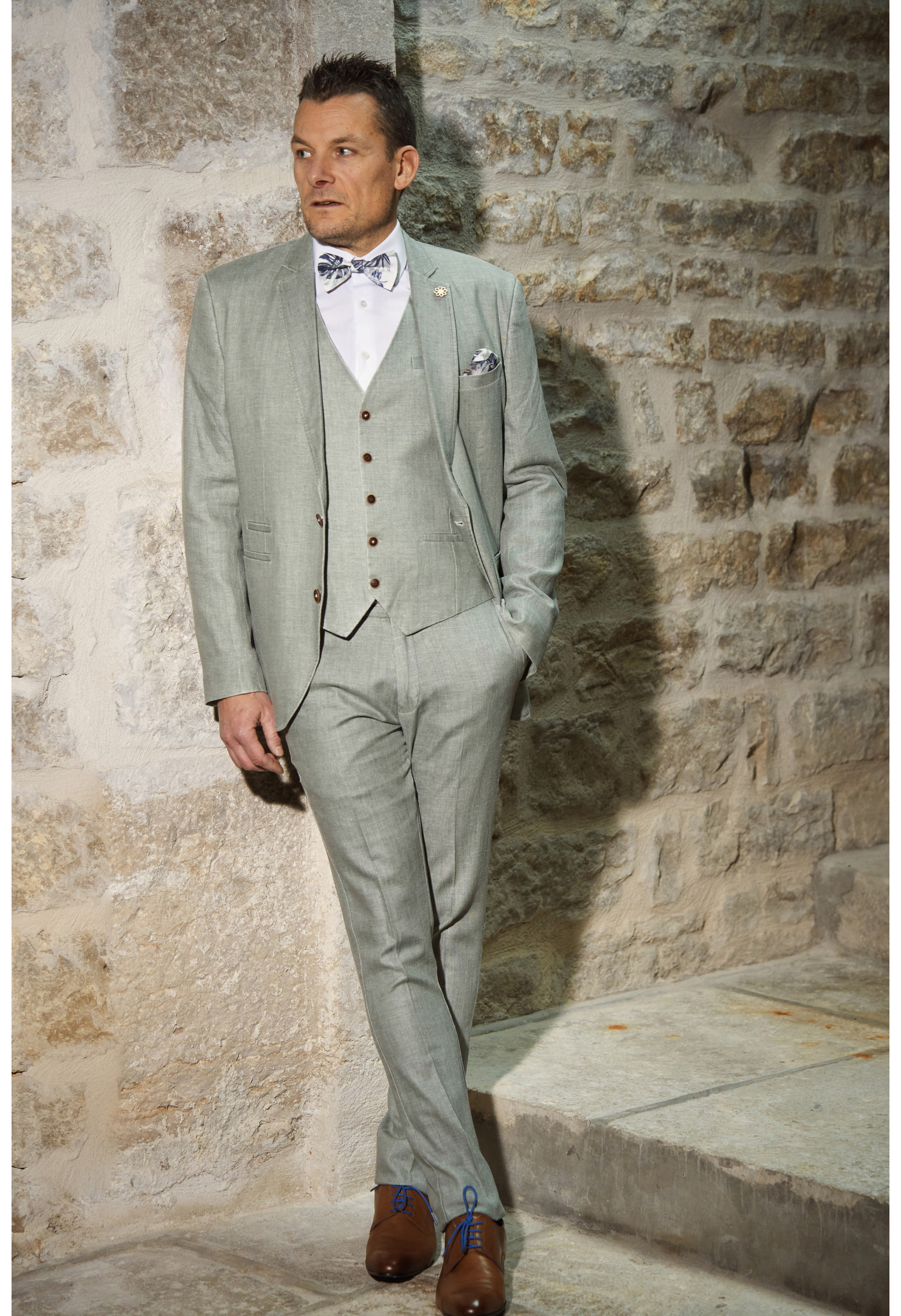 Homme de face en costume GIORGIO céladon  3 pièces contre un mur en pierre.