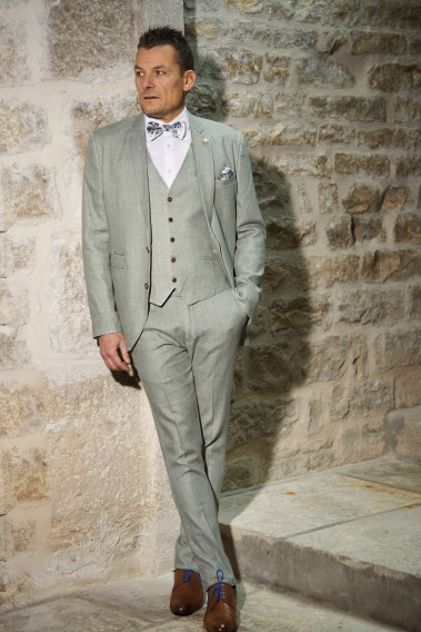 Homme de face en costume GIORGIO céladon  3 pièces contre un mur en pierre.