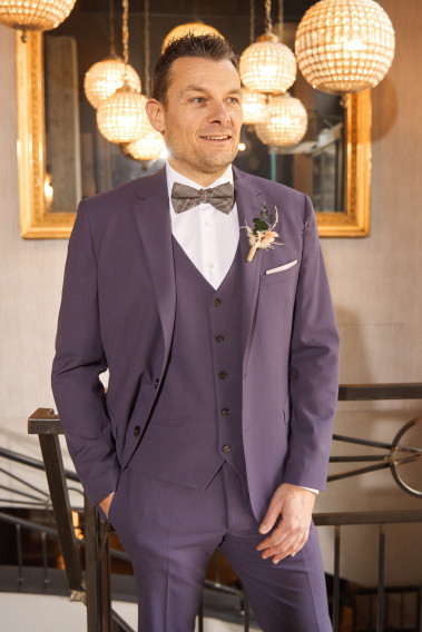 Homme de face en costume SUAT violet 3 pièces une cours. Il porte des chaussures marrons.