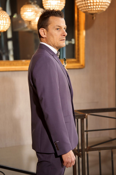 Homme de profil en costume SUAT violet 3 pièces une cours. Il porte des chaussures marrons.