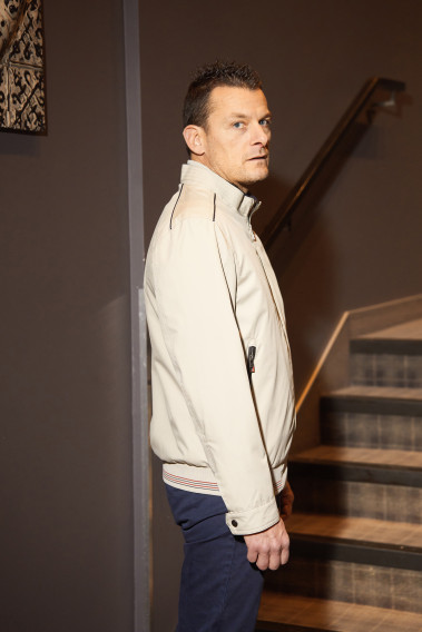 Homme de profil portant le blouson FLAG beige. Il comporte 2 poches repose mains.
