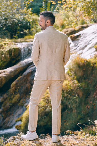 Homme de dos en costume GIORGIO couleur sable 3 pièces sur un rocher. ils porte des baskets blanches.