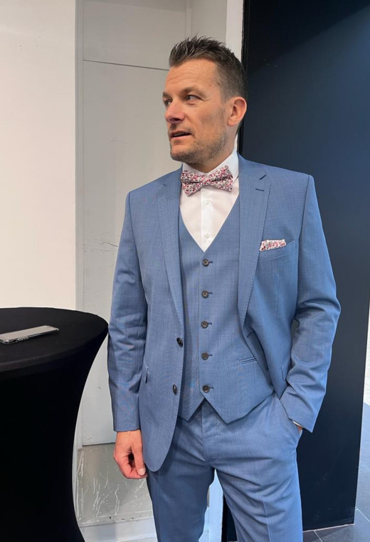 Homme de face en costume SUAT couleur bleu 3 pièces dans une salle.