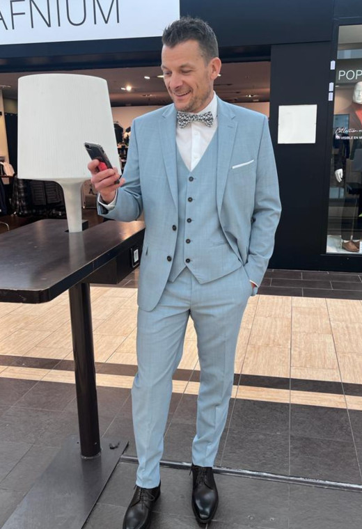 Homme de face en costume SUAT couleur bleu clair 3 pièces devant le magasin. Il porte des chaussures noires.