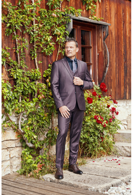 Homme de face en costume CITIZEN bordeaux 2 pièces devant un chalet.