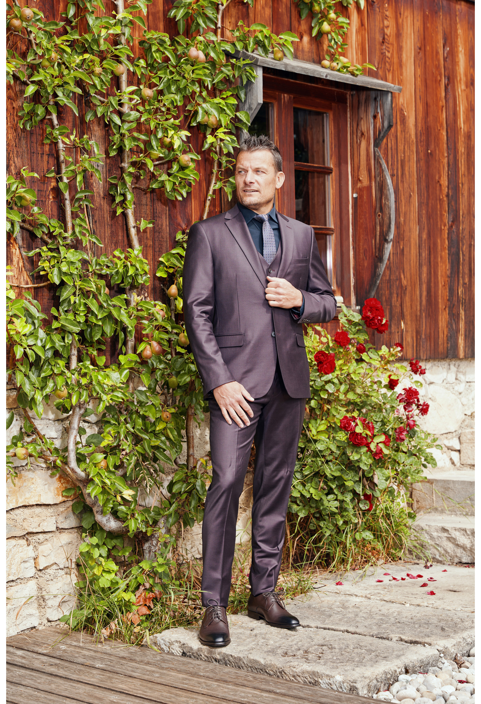 Homme de face en costume CITIZEN bordeaux 2 pièces devant un chalet.