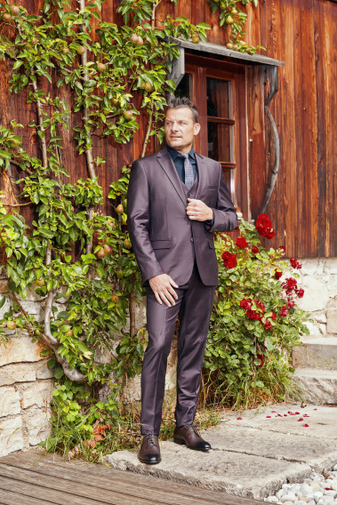 Homme de face en costume CITIZEN bordeaux 2 pièces devant un chalet.