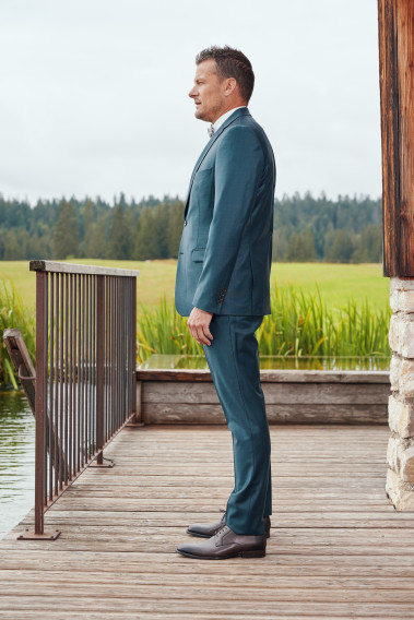 Homme de profil en costume CITIZEN bleu vert 2 pièces. Il porte des chaussures marrons.