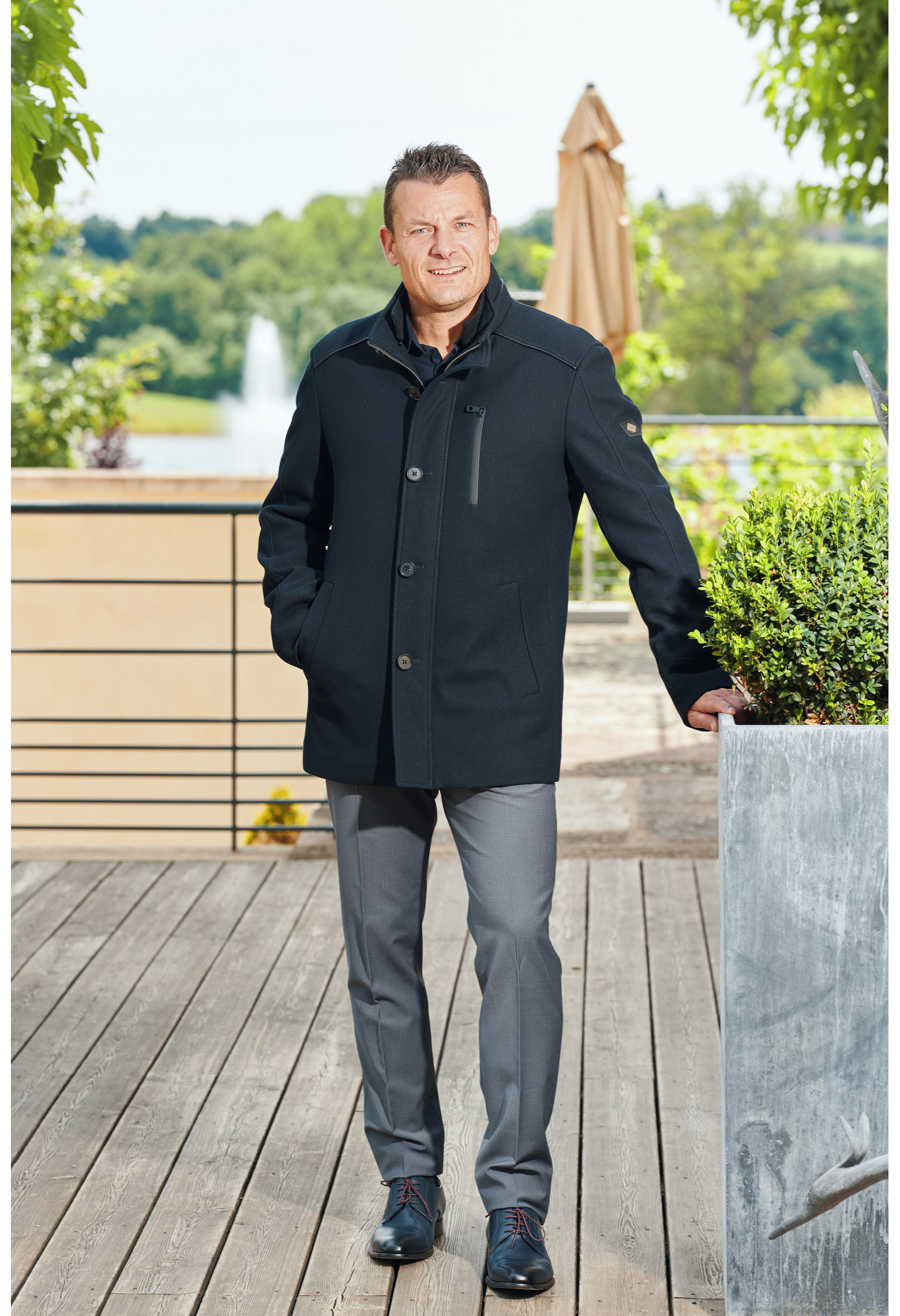 Homme portant le manteau DIVALI marine. Il est court et comporte une poche poitrine et 2 poches repose mains.