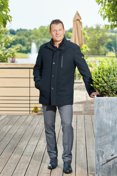 Homme portant le manteau DIVALI marine. Il est court et comporte une poche poitrine et 2 poches repose mains.