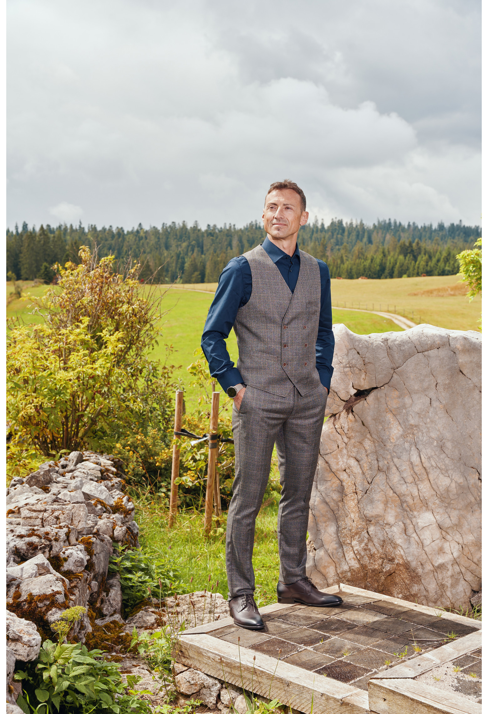 Homme de face portant le gilet PIANOSA carreaux marron. Elle comporte 6 boutons.