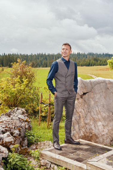 Homme de face portant le gilet PIANOSA carreaux marron. Elle comporte 6 boutons.